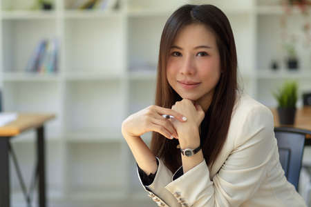 Beautiful and charming Asian businesswoman in white suit sitting and posting at her office workplaceの写真素材