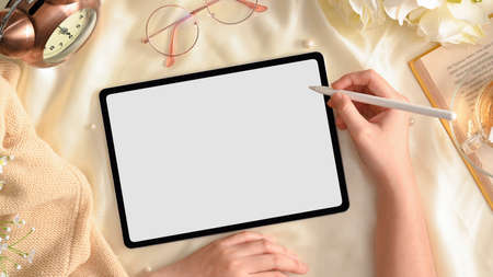Close-up image, A female holding stylus pen and sketching on digital tablet touchpad mockup on feminine workspace. top viewの写真素材