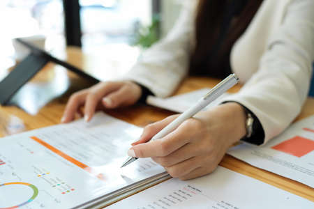 Close-up image and selective focus businesswoman holding a pen, writing or taking notes on financial report paperwork.の写真素材