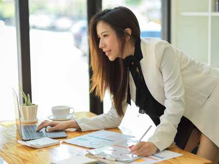 Side shot, Attractive businesswoman leaning on table and working on her financial project in the office.の写真素材