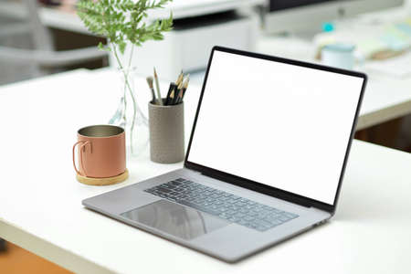 Modern bright workspace with notebook laptop computer blank screen mockup and supplies on table.の写真素材