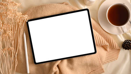 Feminine workspace composition with digital tablet computer white display over cozy warm sweater, coffee cup and accessories on table. top viewの写真素材