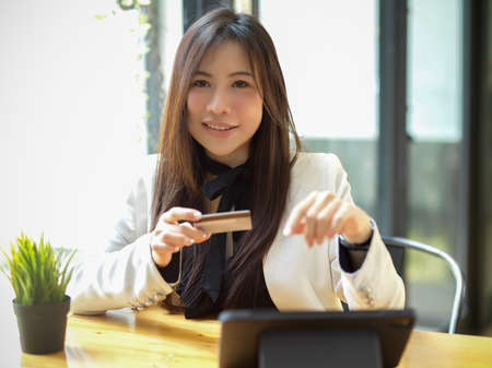 A beautiful young woman in stylish outfit sitting at table and holding a credit card or debit card.の写真素材
