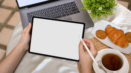 Close-up, Female using digital tablet on outdoor coffee table. Tablet blank screen mockup, laptop,...