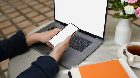 Female sitting at outdoor working space, using smartphone and working on laptop computer. digital devices blank screen mockupの写真素材
