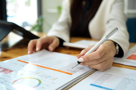 Close-up hands image, A businesswoman or female financial worker analysing financial data report, pointing pen on paperwork.の写真素材