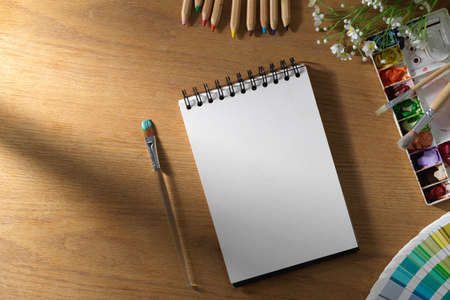 An empty page on spiral notepad or school notebook with painting equipment on wooden tabletop.の写真素材
