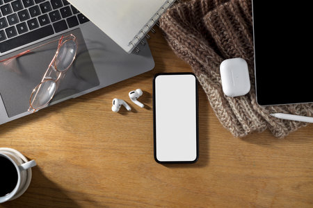 Simple feminine office desk with laptop, earbuds, tablet, stuff and smartphone white screen mockup on wooden table. top viewの写真素材