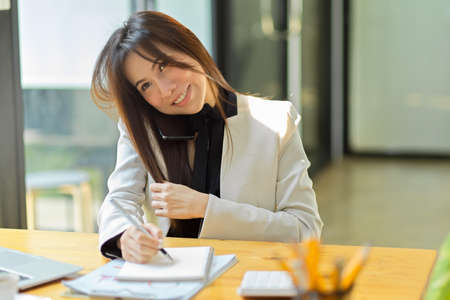 Attractive female assistant or secretary answering phone call and taking notes on her notepad at her...