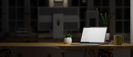 Modern dark office workstation at night concept with laptop computer mockup and copy space on wooden table under light over blurred dark office background. 3d rendering, 3d illustrationの写真素材