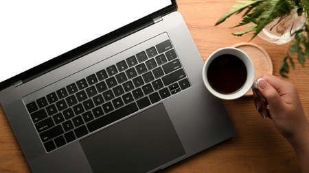 Top view, close-up, A woman working at her office table, sipping black coffee and working on laptop...