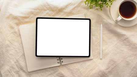 Simple minimal workspace tablet computer white screen mockup with notebook, stylus pen, coffee cup on white tablecloth. top viewの写真素材
