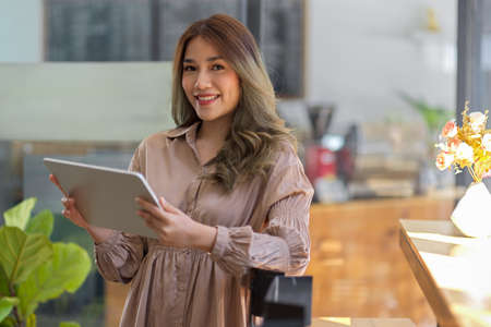 Attractive Asian female in stylish dress and blonde hair holding a modern digital tablet computer in...