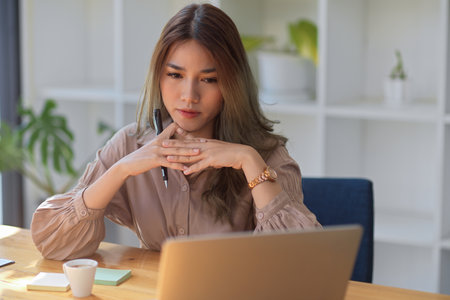 An elegant Asian businesswoman concentrated on her project work on her laptop computer, thinking of ideas to solve the problems.の写真素材