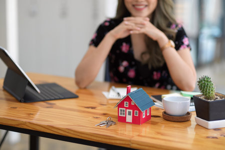 Property investment or house rental concept, A red house model on office desk with blurred real estate agent sitting at table in the background.の写真素材