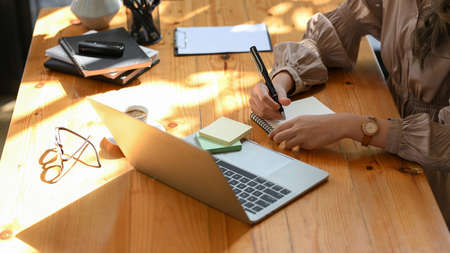 Cropped shot of a businesswoman taking a notes on memo pad, writing some details on sticky notes at...