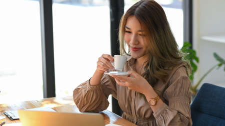 Cheerful attractive asian businesswoman sipping her hot morning espresso coffee shot at cafe.の写真素材