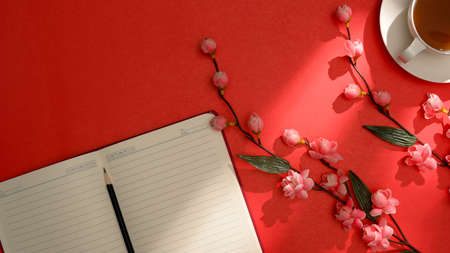 Red workspace background with empty notebook pages, pencil, tea cup and flowers. top viewの写真素材
