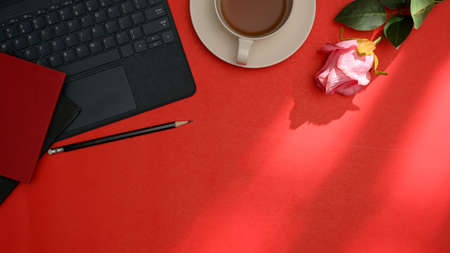 Red office desk with tablet keyboard, coffee cup, notebook, pencil, rose and copy space. top viewの写真素材