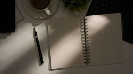 White book mockup pages with a coffee and workspace accessories on white table under sunlight shadowの写真素材