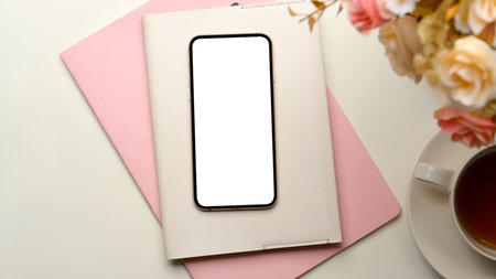 Female home office workspace with empty smartphone screen mockup, books, flowers and tea cup on white background.の写真素材