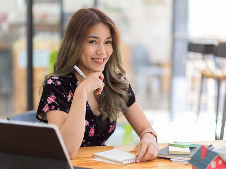 Elegant asian young college student doing her homework assignment in a coffee shop workspace. Businesswoman sitting at her office desk.の写真素材
