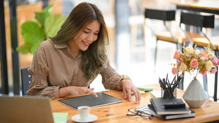 Cheerful woman using portable tablet computer in the coffee shop. Female freelancer working on tablet and sitting in the cafe.の写真素材