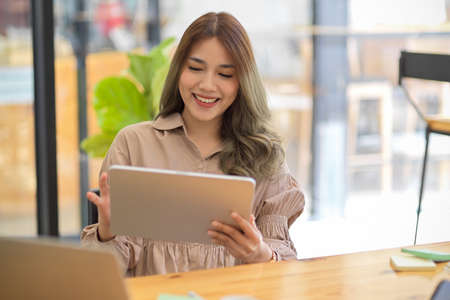 Positive asian woman using a portable digital tablet touchpad computer, sitting at a coffee table in the coffee shop.の写真素材