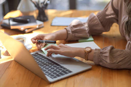 Cropped image, a female hands typing on notebook laptop keyboard on a wooden office desk.の写真素材