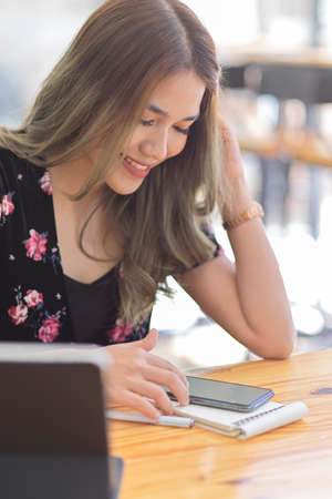 Portrait of a Beautiful asian university student in causal dress waiting friends in coffee shop and playing mobile game on table.の写真素材