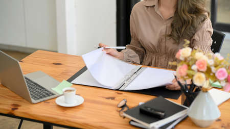 Cropped shot, female manager or businesswoman checking and summarise the informations on document binder, sitting at her office table.の写真素材