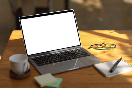 Close-up shot, Simple wooden office desk with laptop computer white screen mockup, coffee mug, and stationery.  remote work, co-working space.の写真素材