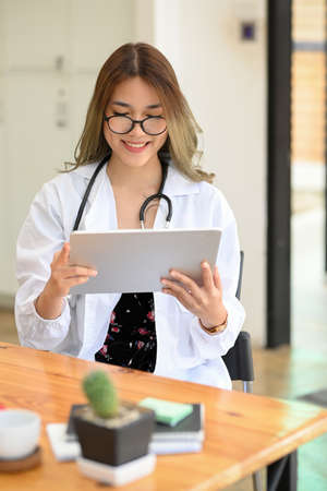 Portrait, Gorgeous asian female doctor sitting at her office desk and checking medical history record report on digital tablet computer.の写真素材