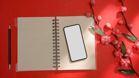 Feminine office table with flowers, pencil, smartphone white screen mockup on empty notebook pages over red background. top view, flat layの写真素材