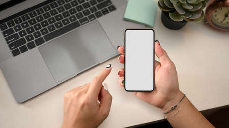 A woman holding mobile phone showing white screen over modern office desk. Top viewの写真素材