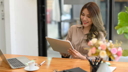 Portrait of Happy Asian young entrepreneur woman using her digital tablet while sitting in the office.の写真素材