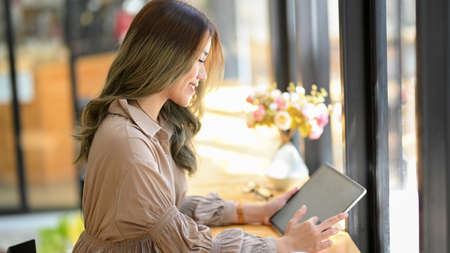Side view, A gorgeous Asian woman relaxing in a modern cafe and enjoy using her portable tablet touchscreen.の写真素材