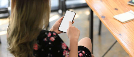 A beautiful female in stylish dress sitting at her office table and enjoy using smartphone. phone screen mockup.の写真素材