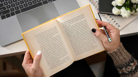 Female reading a novel book at her home office. Woman looking for some informations on notebook. top viewの写真素材