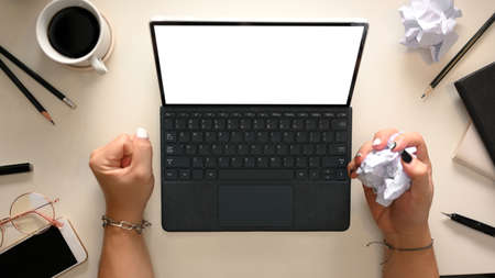 A female employee is dissatisfied with her work report, working on a tablet computer with a crumpled piece of paper in her hand and on the office table. top viewの写真素材
