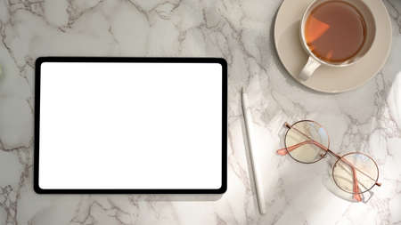 Feminine office desk or portable workspace with tablet blank screen mockup, eye-glasses and teacup on marble background. flat lay, top viewの写真素材