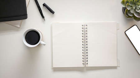 Overhead, Modern white workspace with coffee cup, stationery, smartphone and empty notebook pages.の写真素材