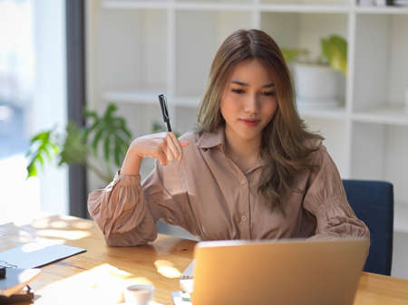 Confident and beautiful asian businesswoman concentrated and focused on her project work at laptop screen in the office.の写真素材
