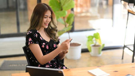Charming and gorgeous Asian woman sits, relaxes in cafe and using her modern smartphone. People with...