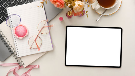 Female beauty blogger workspace with laptop, flowers, teacup, makeups, notebook and digital tablet white screen mockup on white background. top view, flat layの写真素材