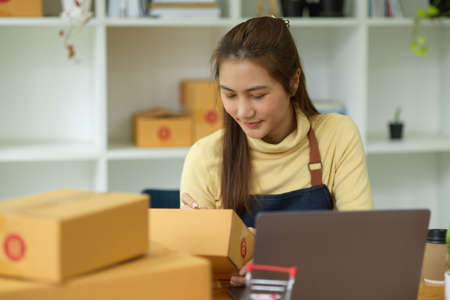A beautiful female entrepreneur or business start up owner prepare packing a delivery package of her customers. Shipping and e-commerce concept.の写真素材