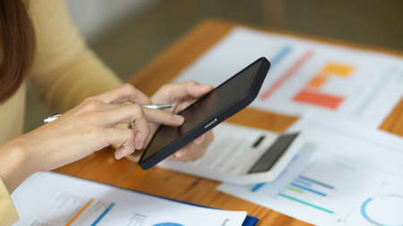 Cropped image, A female financial worker doing finance work and using smartphone over the table in office.の写真素材