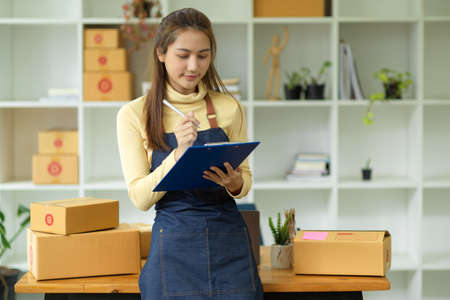 Portrait, attractive asian young female startup business owner looking at report on clipboard, checking her product stocks in her home office. Online seller, Small business entrepreneur.の写真素材