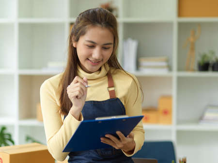 A lovely Asian female small business owner checking her best seller and ready for shipment stock report on her clipboard.の写真素材