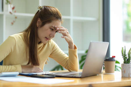 A stressed-out businesswoman sits in front of her laptop screen, worried and dissatisfied with her work project.の写真素材